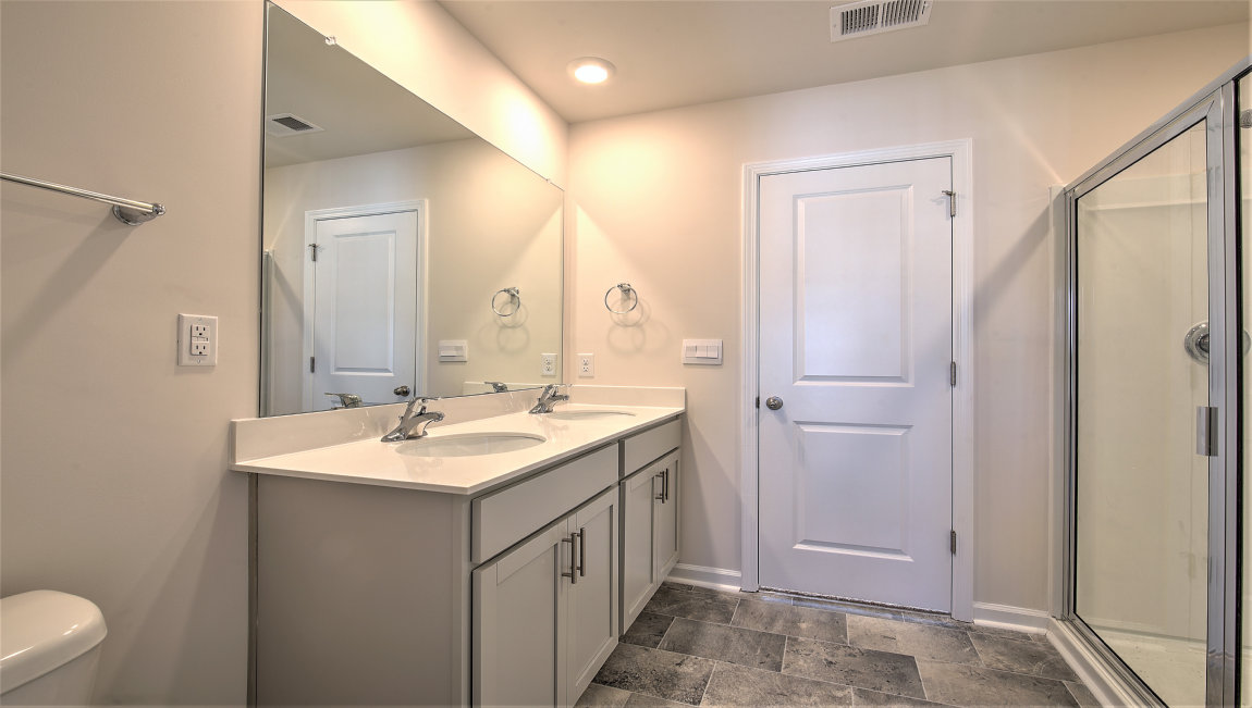 Primary bathroom with double vanity, white counters and cabinets and glass door shower