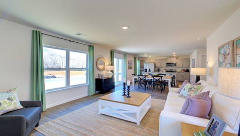 Great room with view of kitchen, has large windows and is against staircase