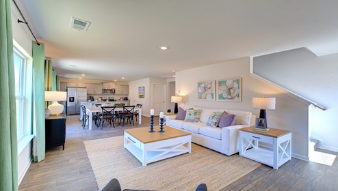 Great room with view of kitchen, has large windows and is against staircase