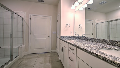 Bathroom with double sinks, white cabinets, and glass door shower