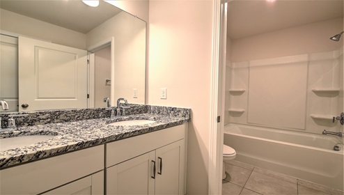 Bathroom with double sinks, white cabinets, and separate door with toilet and bathtub