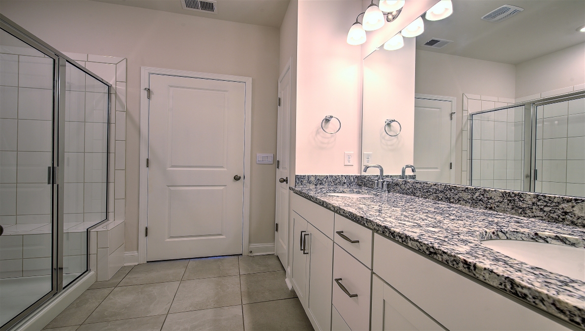Bathroom with double sinks, white cabinets, and glass door shower