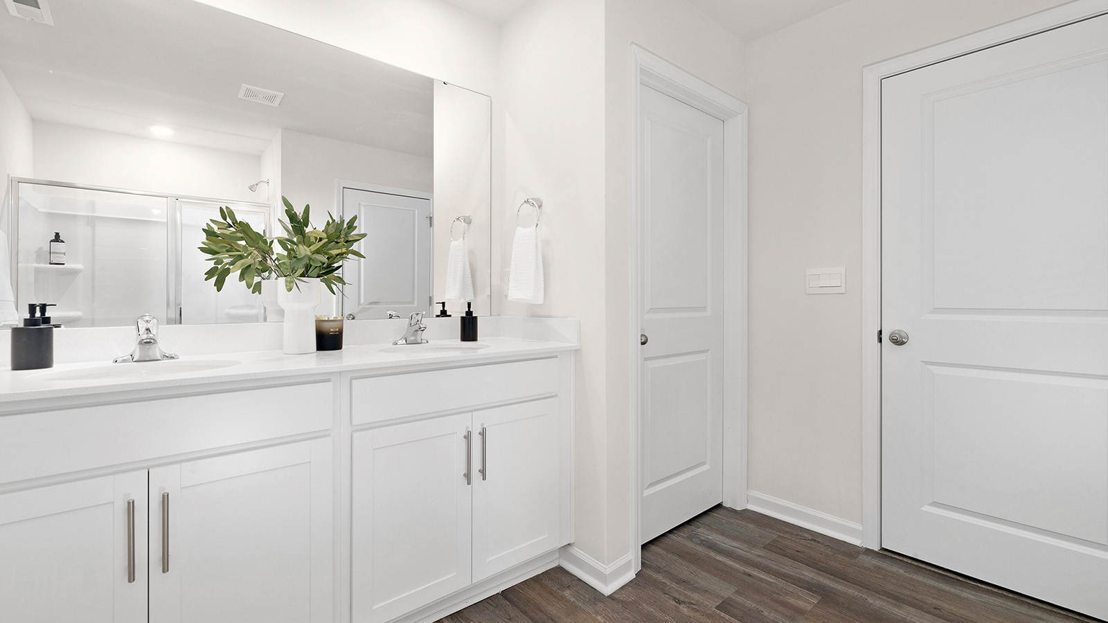 Primary bathroom with double vanity, white cabinets and standing glass door shower