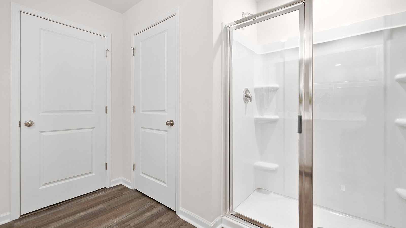 Primary bathroom with double vanity, white cabinets and standing glass door shower