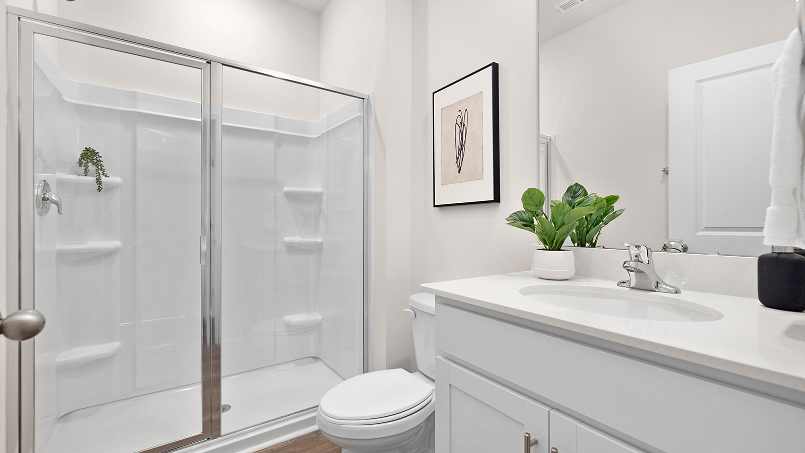 Primary bathroom with double vanity, white cabinets and standing glass door shower