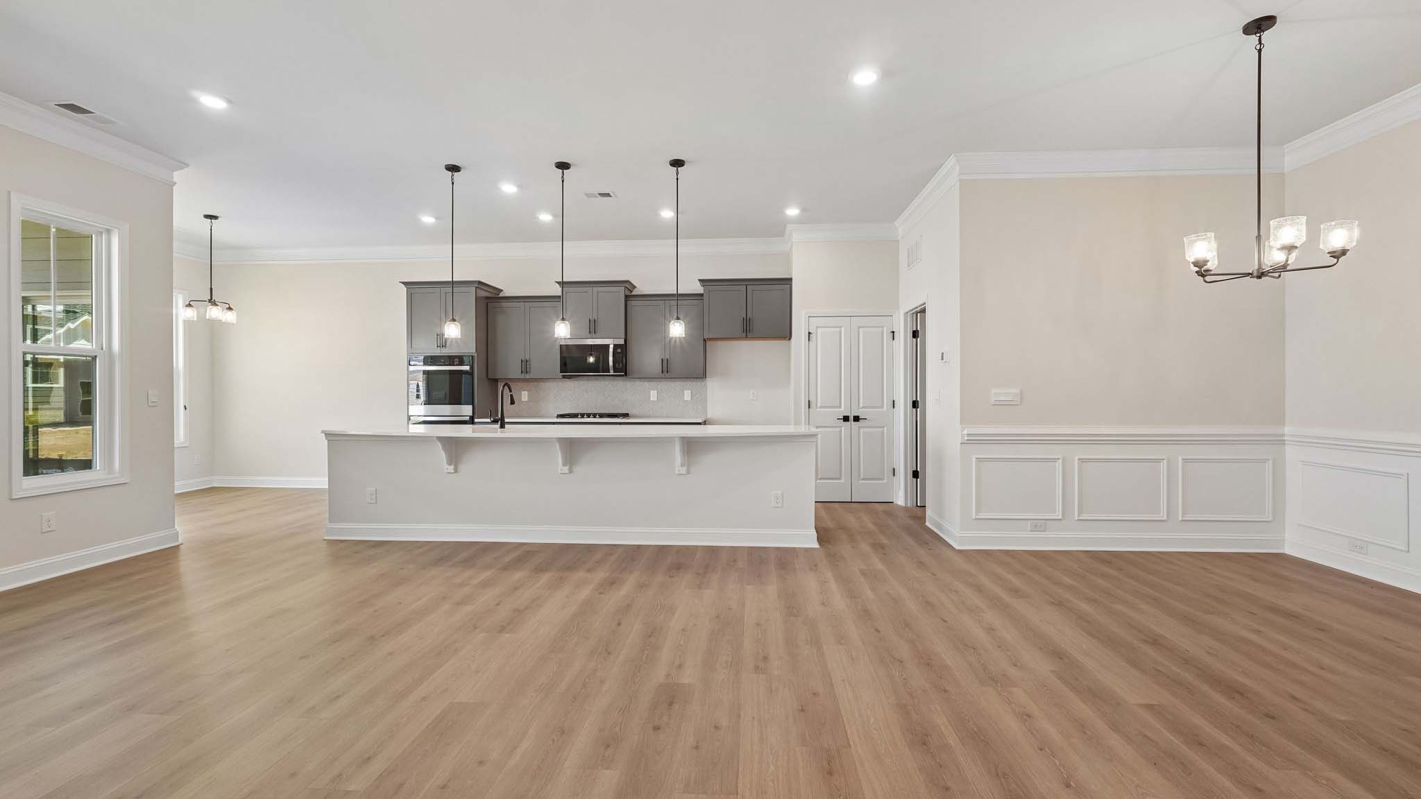 Kitchen and island with wood floors, white cabinets and counters, stainless steel appliances, and seating at island bar