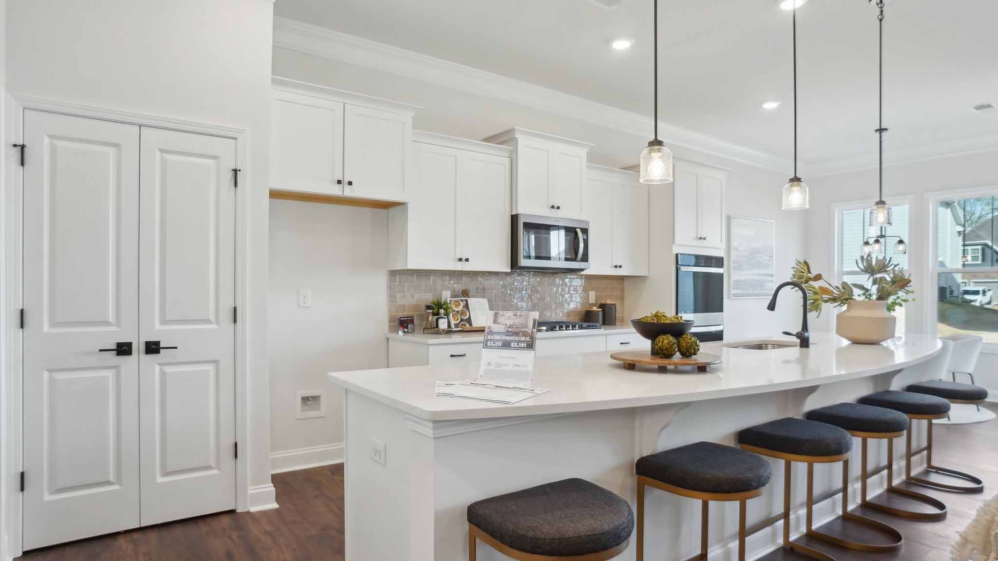 Kitchen and island with wood floors, white cabinets and counters, stainless steel appliances, and seating at island bar