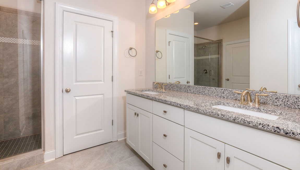 Primary bathroom with two sinks and counters, white cabinets, and wood floors