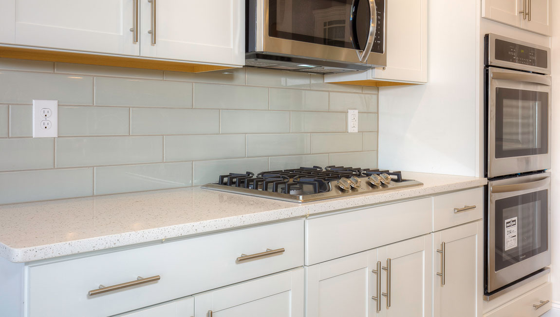 Kitchen and island with wood floors, white cabinets, quartz counters, and stainless steel appliances