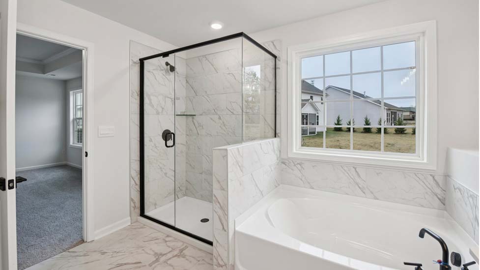 Primary bathroom with white cabinets, bathtub, and glass door shower
