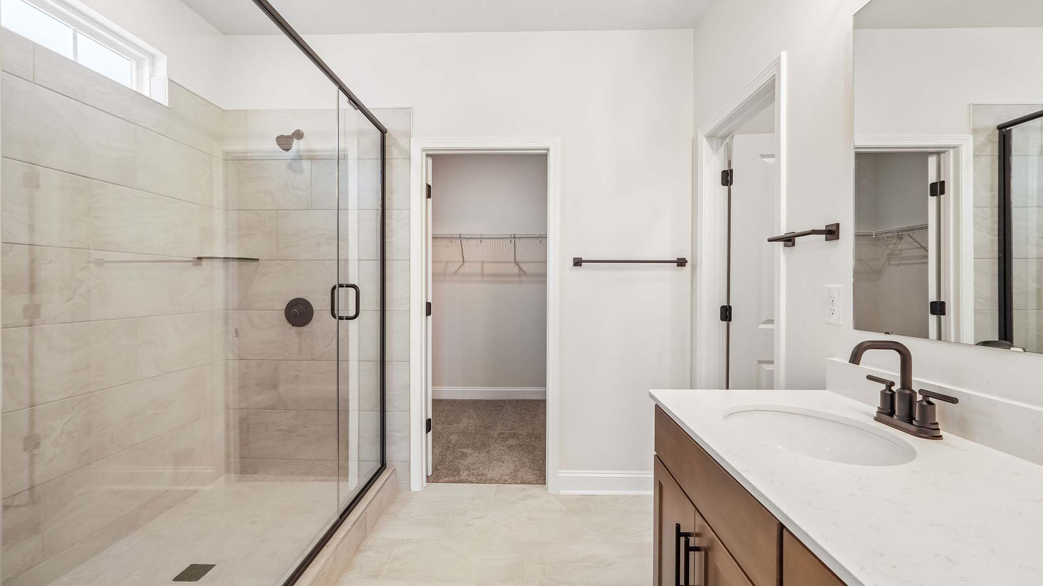 Primary bathroom with white cabinets, double sinks, and glass door shower