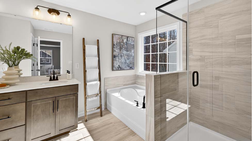 Primary bathroom with double sinks, brown cabinets and bathtub and glass door shower combination