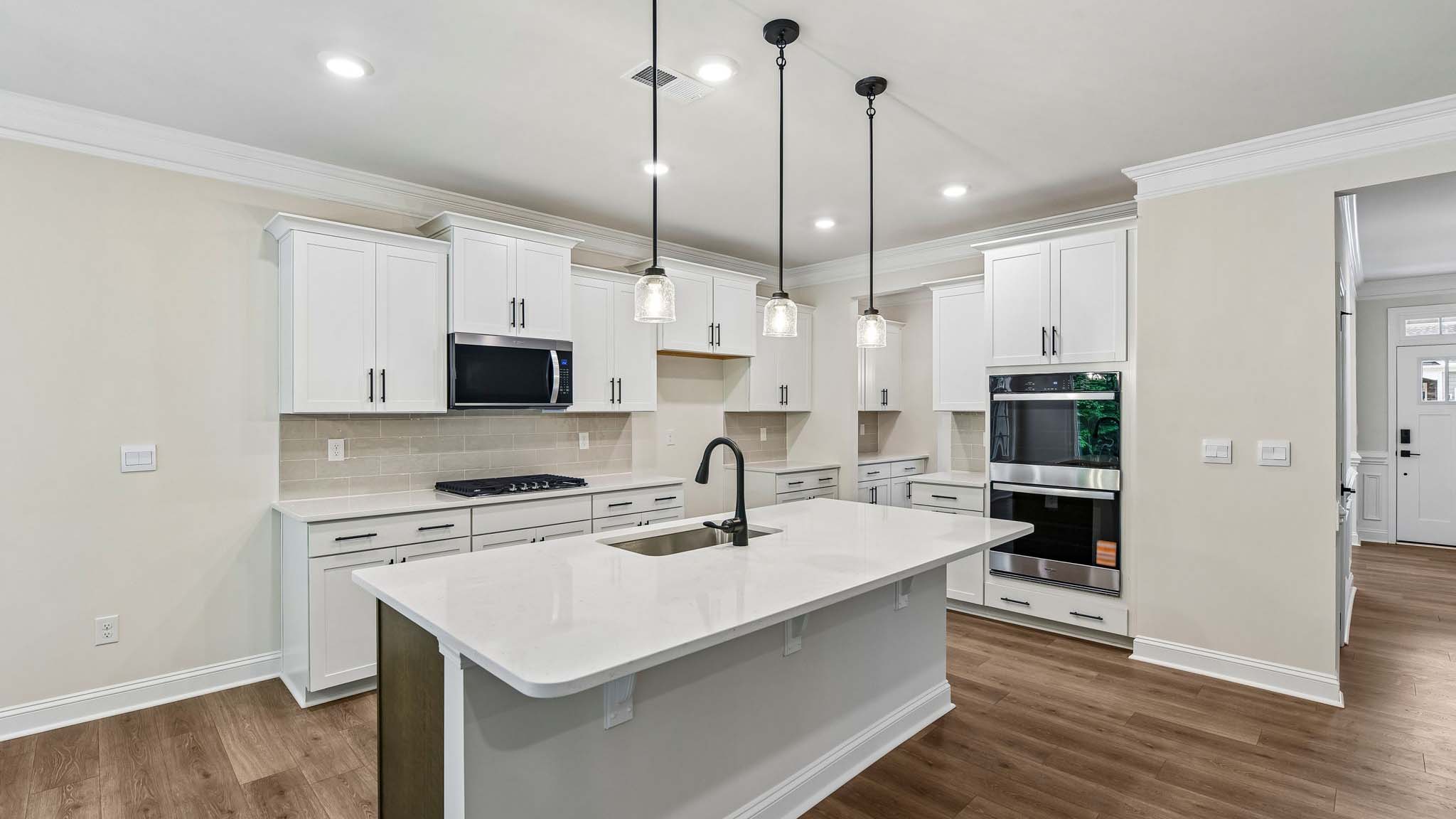 Kitchen and island with white cabinets and counters, wood floors, and stainless steel appliances