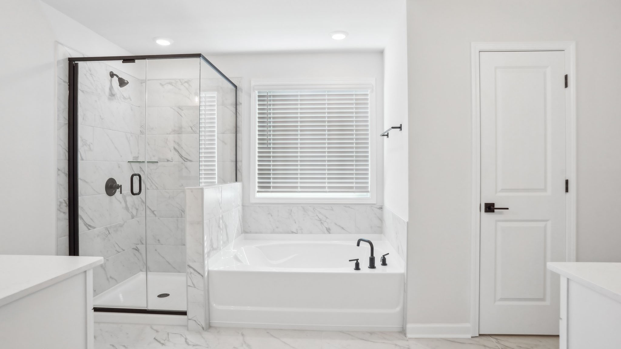 Primary bathroom with double sink vanity, brown cabinets, large bathtub, and separate standing glass door shower