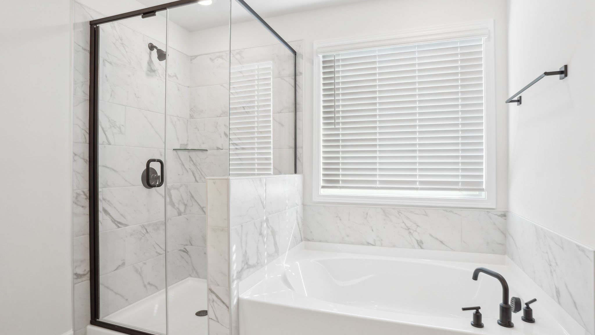 Primary bathroom with double sink vanity, brown cabinets, large bathtub, and separate standing glass door shower