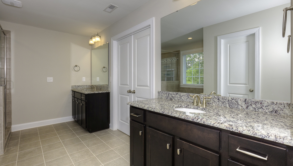 Primary bathroom with double sink vanity, brown cabinets, large bathtub, and separate standing glass door shower