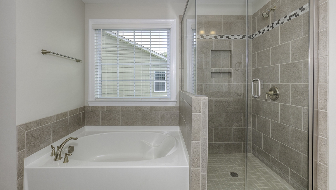 Primary bathroom with double sink vanity, brown cabinets, large bathtub, and separate standing glass door shower