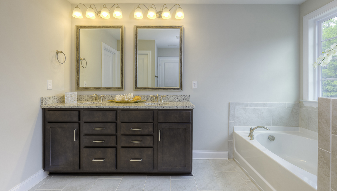 Primary bathroom with brown cabinets, double sinks, and separate bathtub and standing glass door shower