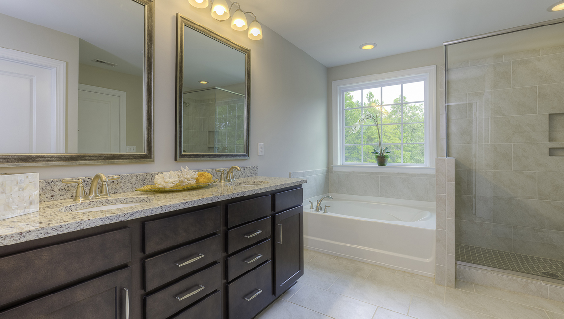 Primary bathroom with brown cabinets, double sinks, and separate bathtub and standing glass door shower