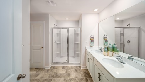 Primary bathroom with double sinks, white counters, and cabinets, glass door shower