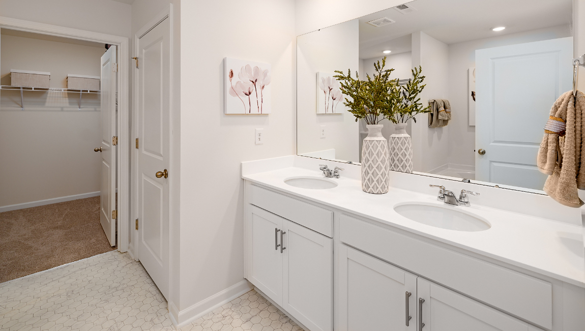 primary bathroom with double sinks, white counters and cabinets, and view of walk in closet