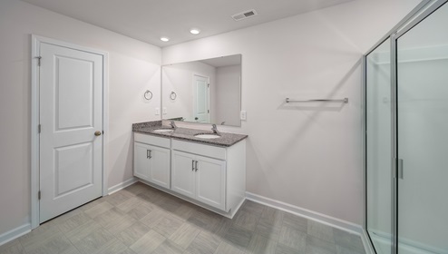 Primary bathroom with double sinks, white cabinets and glass door shower