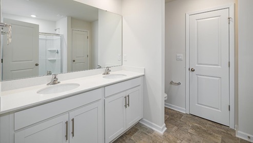 Primary bathroom with double sinks, white counters and cabinets, and glass door shower