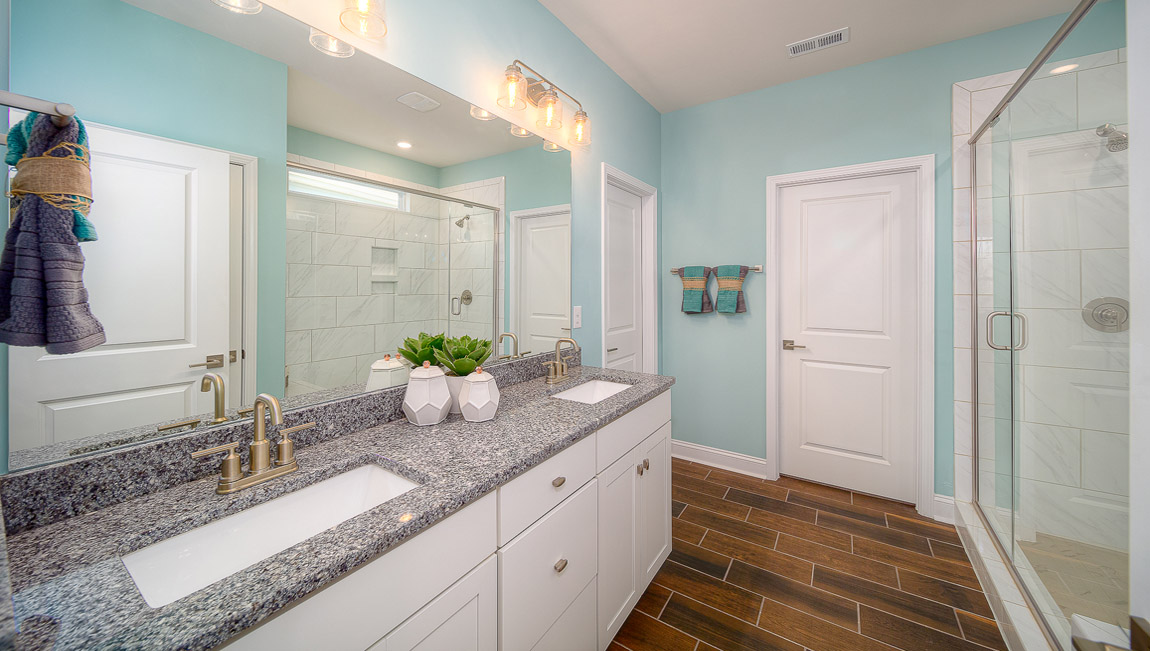 Primary bathroom with white cabinets, double sinks, and glass door shower