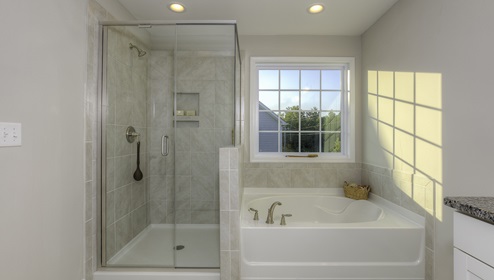 Primary bathroom with white cabinets, double sinks, and bathtub and glass door shower combination