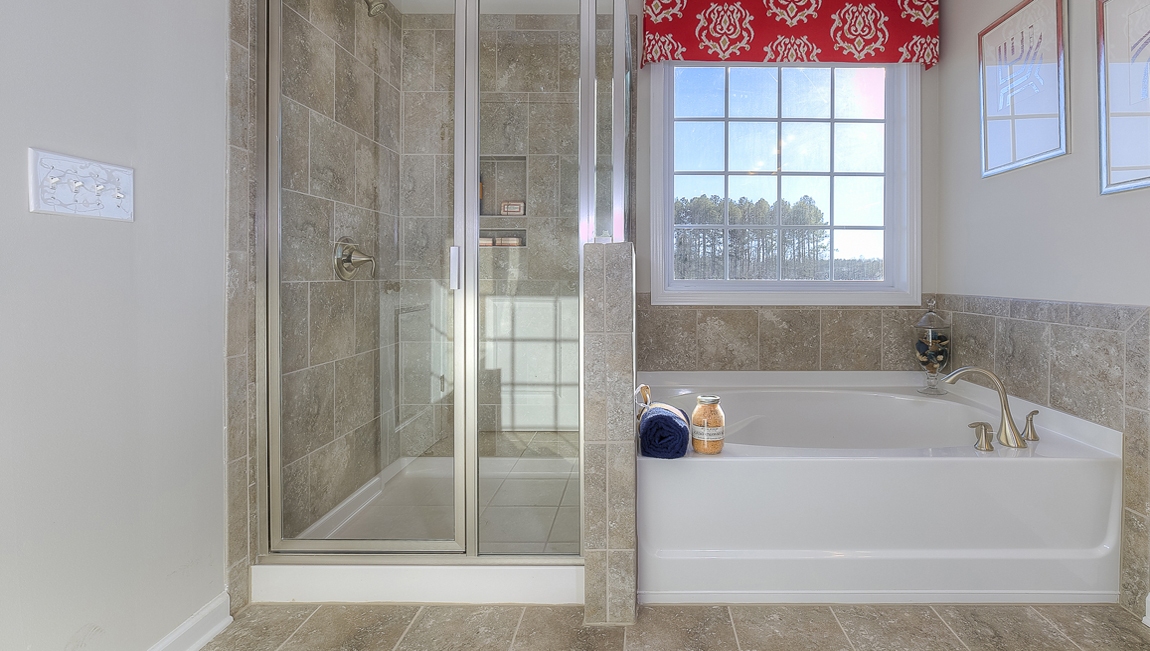 Primary bathroom with double sinks, brown cabinets and bathtub and glass door shower combination