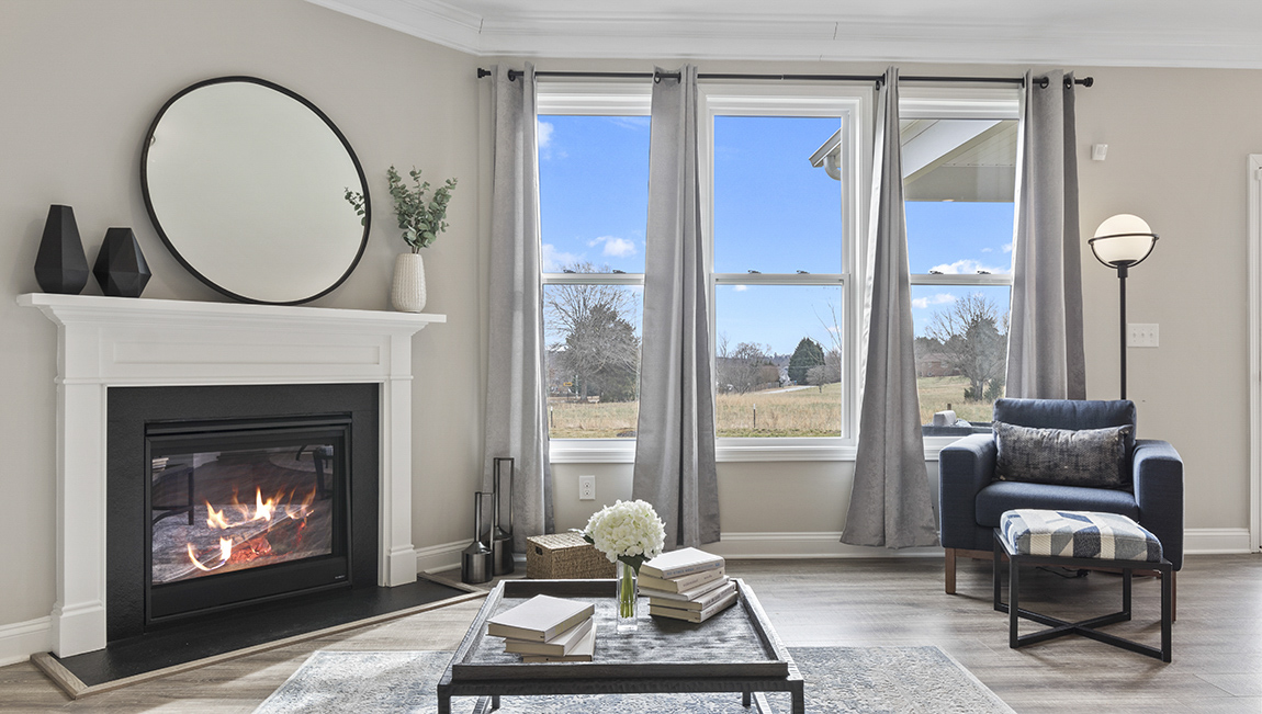 Living room space beside kitchen with wood floors and fireplace, and three large windows