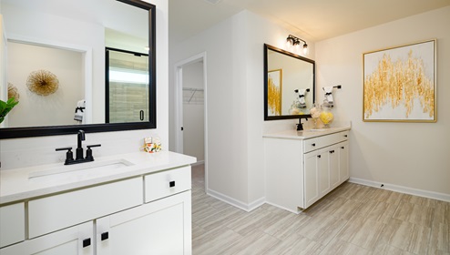 Primary bathroom with two sinks and counters, white cabinets, and wood floors