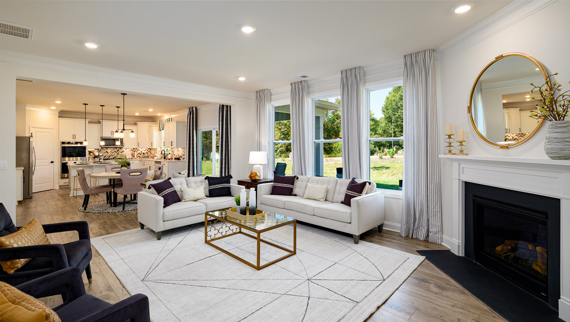 Open concept family room with wood floors, 3 large windows, and fireplace, view of kitchen in distance