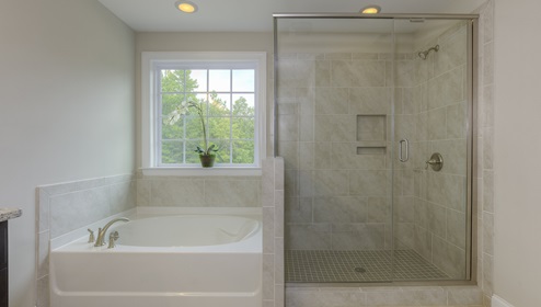 Primary bathroom with brown cabinets, double sinks, and separate bathtub and standing glass door shower