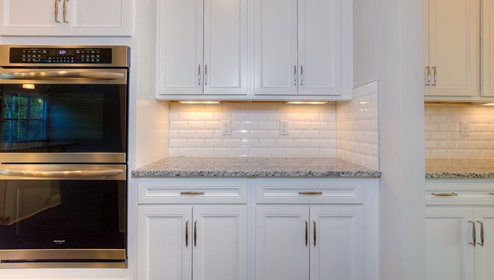 Butlers pantry with white cabinets and white subway tile backsplash beside ovens