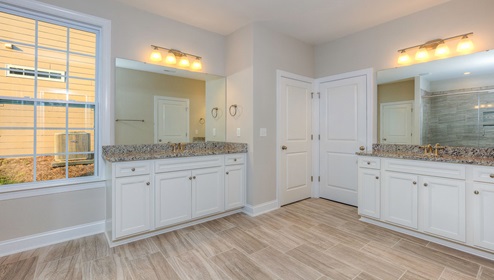 Primary bathroom with two vanities, white cabinets and large glass door shower
