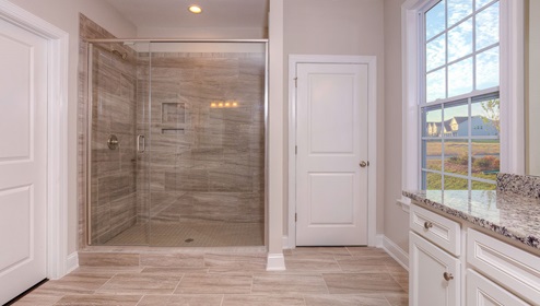 Primary bathroom with two vanities, white cabinets and large glass door shower
