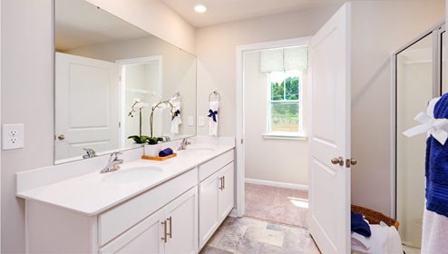 Azalea Ridge Model primary bathroom with white cabinets and counters, double sinks, and glass door shower