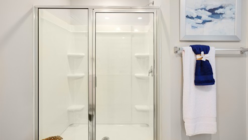 Model primary bathroom with white cabinets and counters, double sinks, and glass door shower