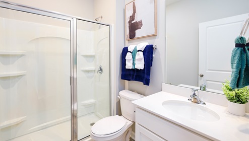 Model bathroom with white counters and cabinets, double sinks and glass door shower