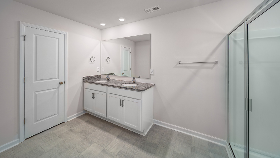 Primary bathroom with double sinks, white cabinets and glass door shower