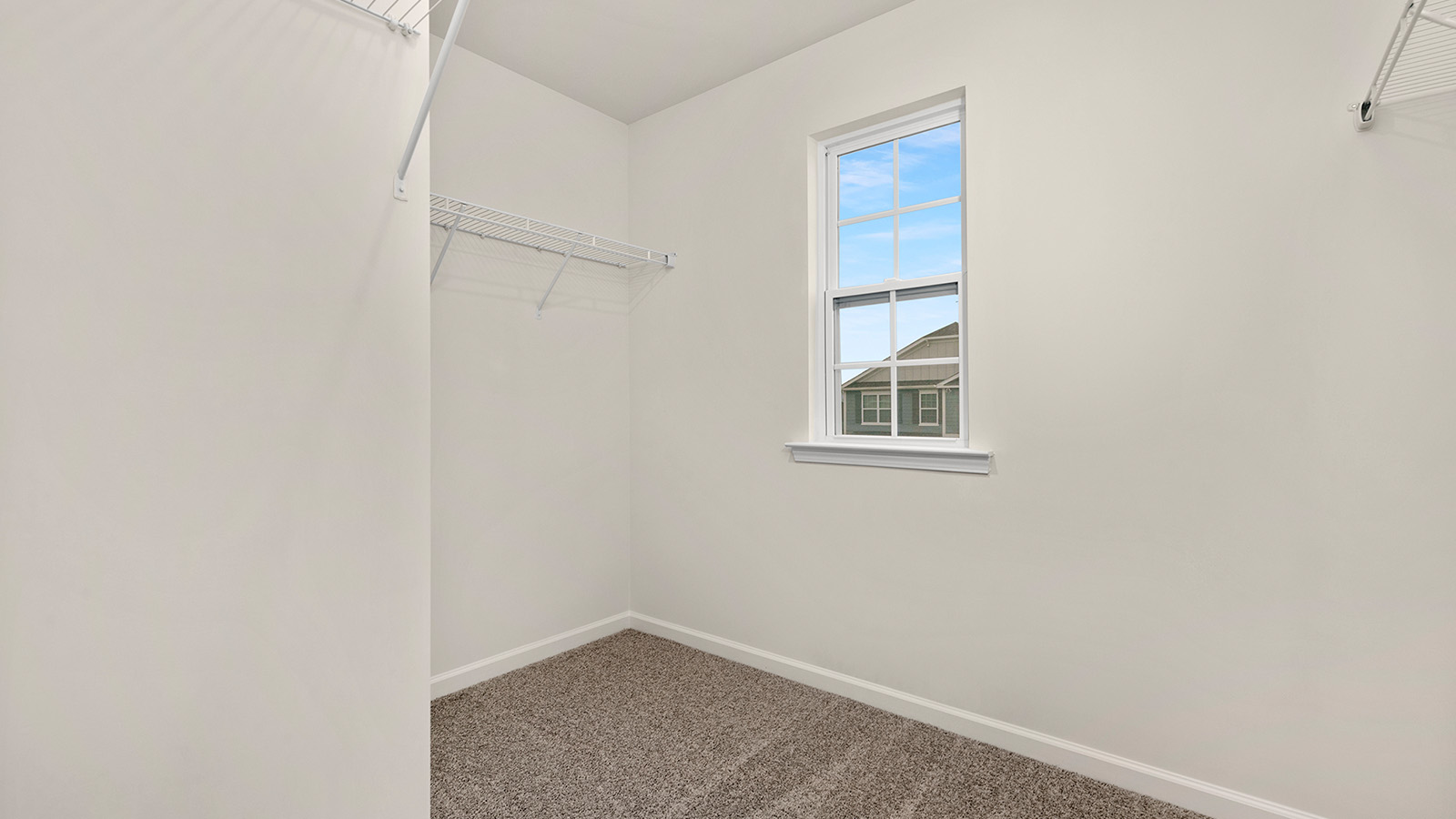 Primary bedroom walk in closet, carpeted, with small window