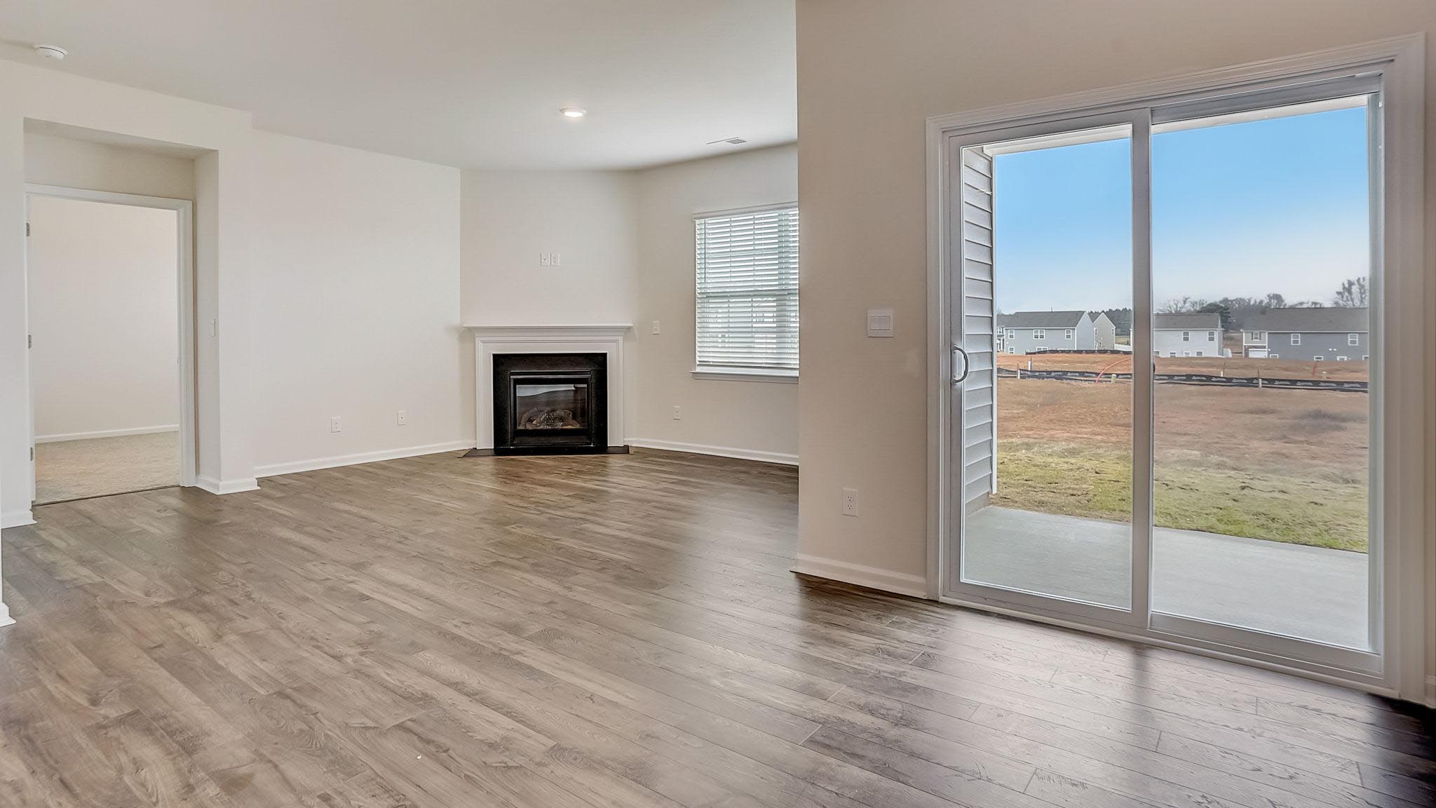 Open living room with wood floors, large window, and fireplace beside dining area