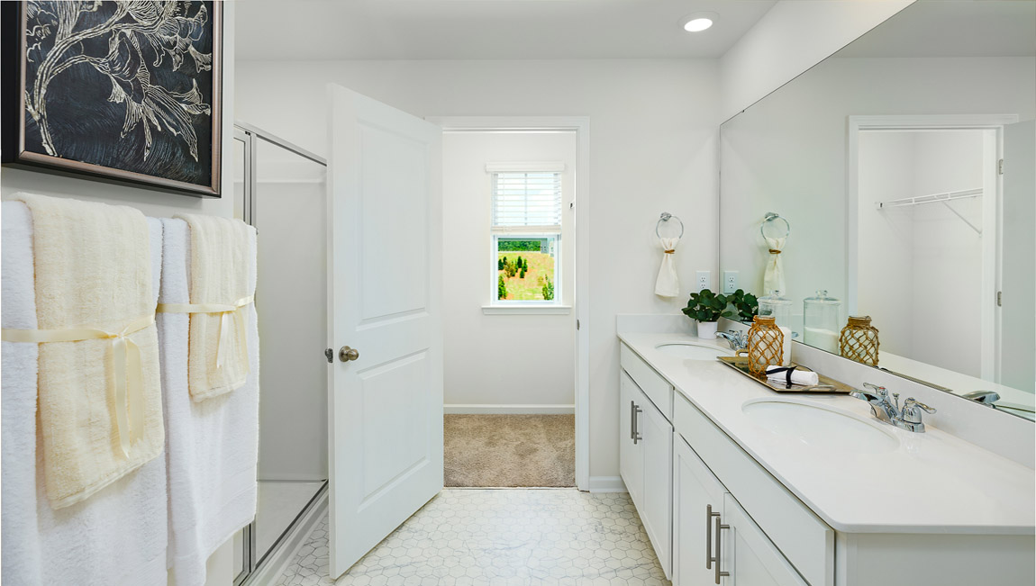 Primary bathroom with white cabinets and counters, double sinks, and glass door shower