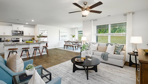 Open living room with ceiling fan and large window, kitchen and dining room in view. New Home in Charlotte, North Carolina