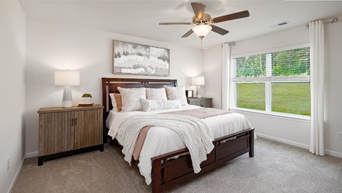 Carpeted primary bedroom with large window and ceiling fan. New Home in Charlotte, North Carolina
