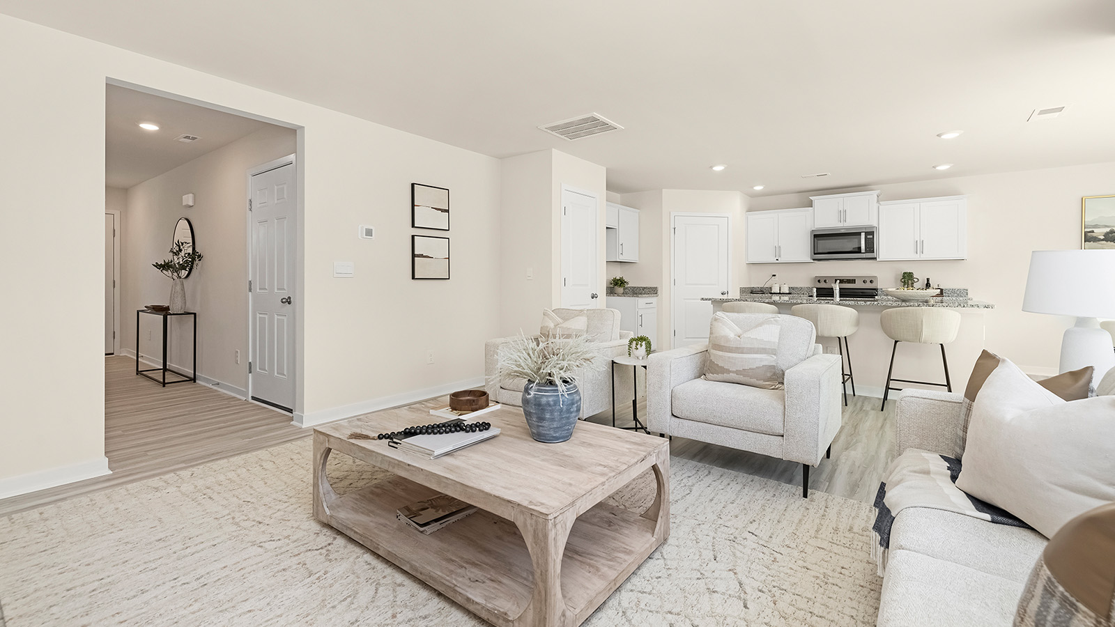 Living room space with wood floors, three large windows and view of kitchen