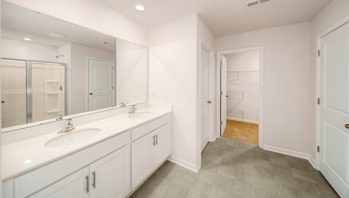 Primary bathroom with double sinks, white counters, white cabinets, and glass door shower