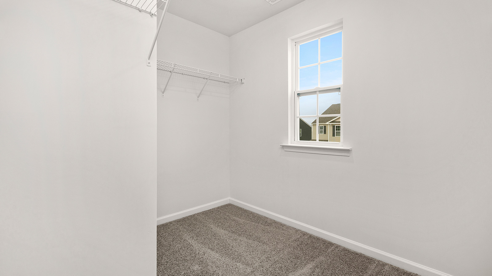 Primary bedroom walk in closet, carpeted, with small window