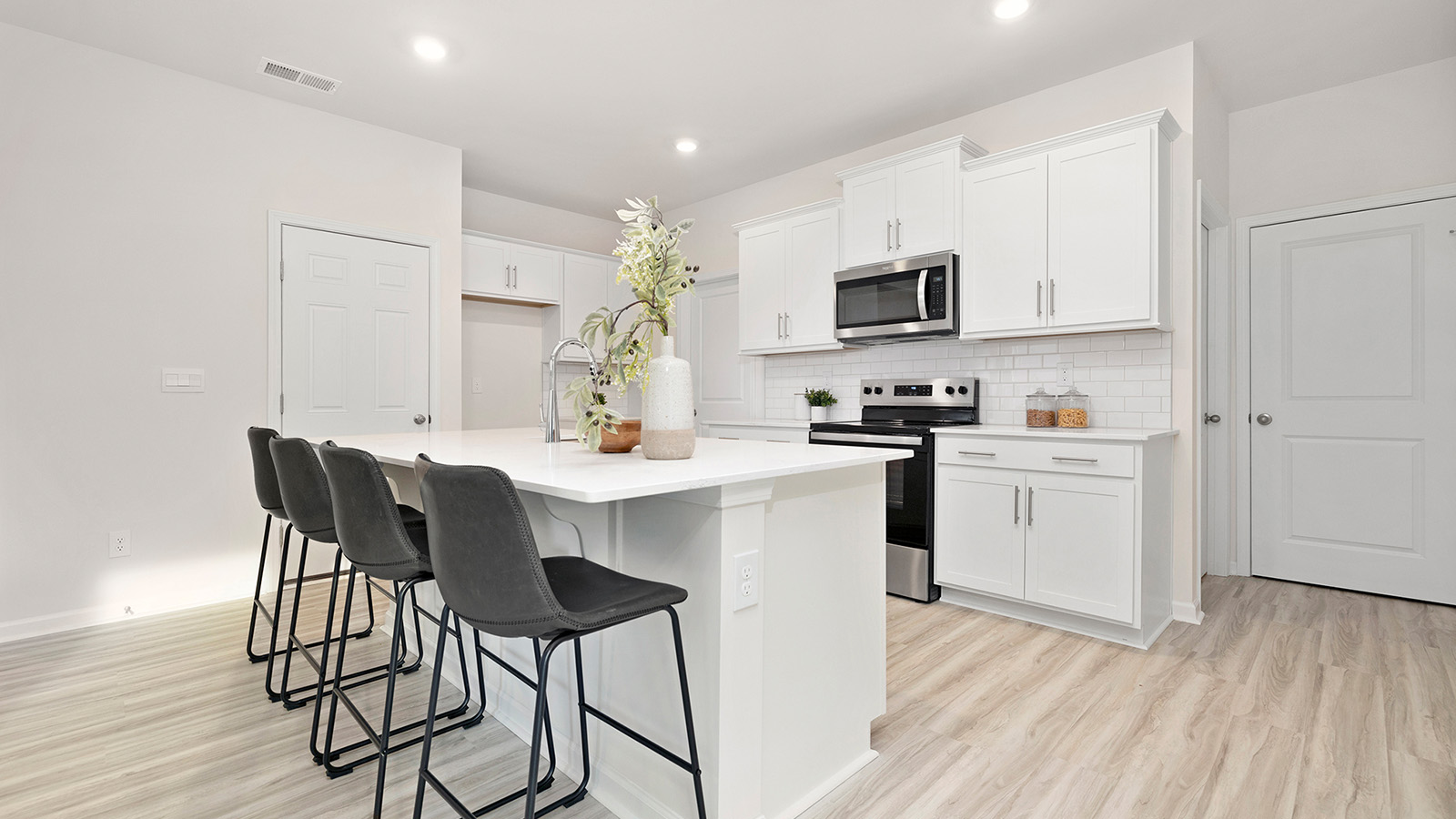 Kitchen and island with white cabinets, counters, subway tile backsplash and stainless steel appliances